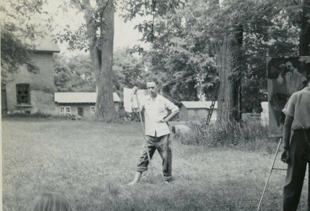 The coach house and bath house can be seen in the background of this photograph, with Jim Gordaneer posing for a demonstration by York Wilson. Jim was one of the students who lived on the upper floor of the coach house during the summer.